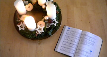 Adventkranz mit entzündeter 1. Kerze und Gesangbuch EM aufgeschlagen bei Lied 138 "Komm, du lang ersehnter Jesus"