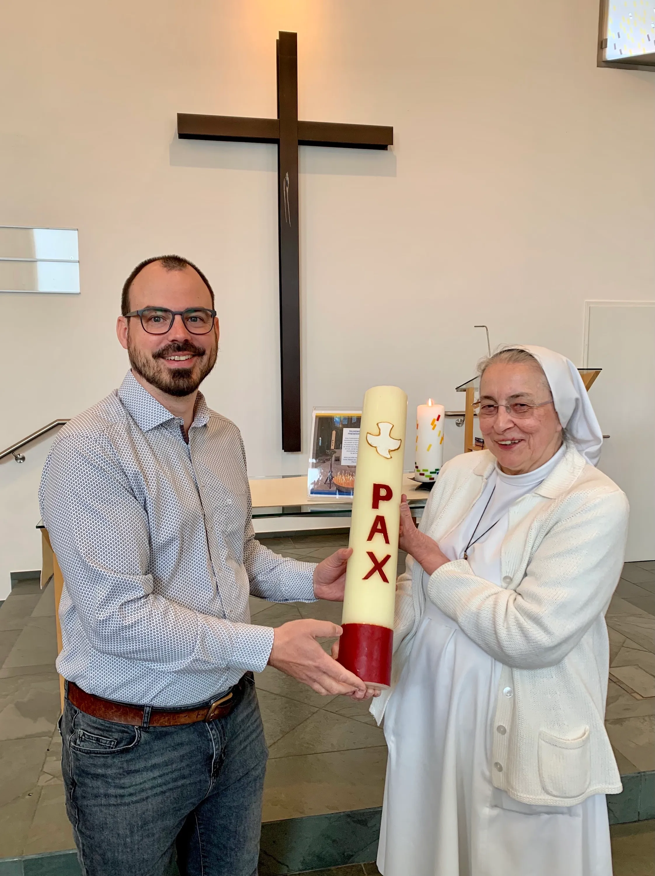 Pastor Martin Obermeir-Siegrist (links) empfängt von Sr. Bernadette (Kreuzschwestern) die Ökumenische Friedenskerze, die im Mai 2023 in der EmK Linz für den Frieden brennt